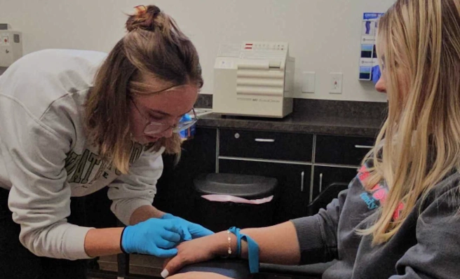 {{ school.name }} student training to apply an IV to a patient