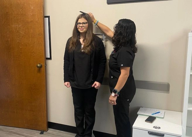 {{ school.name }} student measuring the height of another student