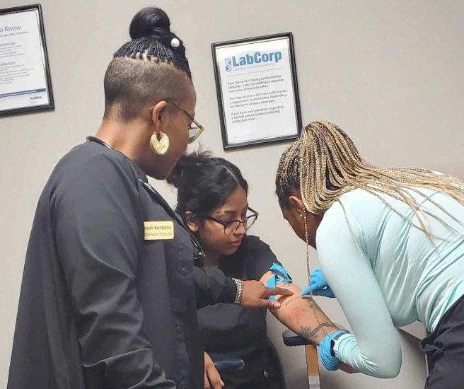 {{ school.name }} students training to take blood draws with their instructor nearby