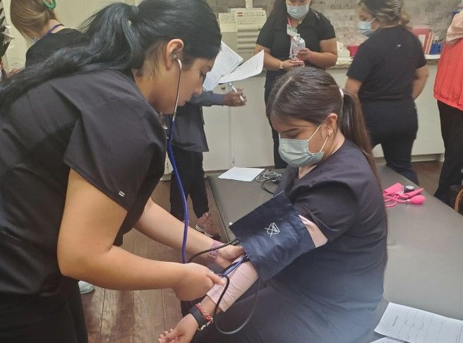 {{ school.name }} students training to take blood pressure from patients
